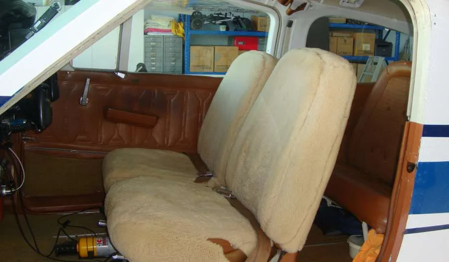 The interior cabin of an aircraft with two beige sheepskin-covered seats and brown side panels.