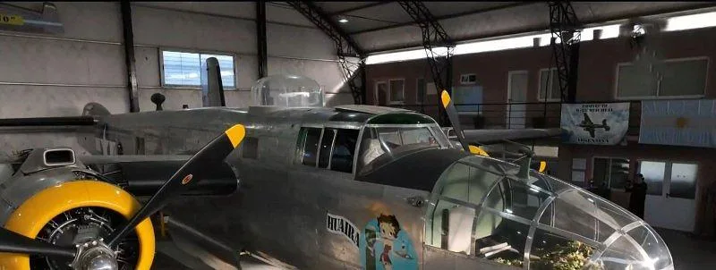 A close-up front-right view of a silver B-25 Mitchell bomber with yellow propeller hubs, parked in a hangar.