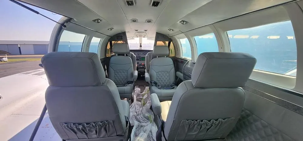 A wide view of the aircraft cabin interior with light gray quilted leather seats and a glimpse of the cockpit instruments.
