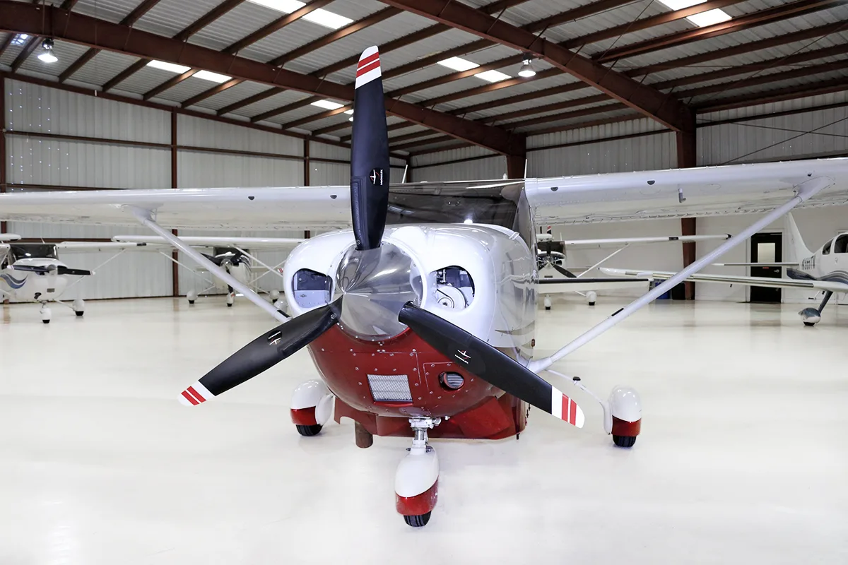 A head-on view of the propeller and nose of a white and red Cessna Stationair TC N6206X in a hangar.