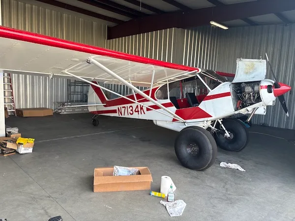 A red and white high-wing bush plane with large tundra tires sits in a hangar with its engine cowling open.