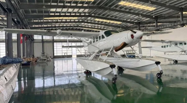 A white floatplane with pontoons is parked inside a large hangar.