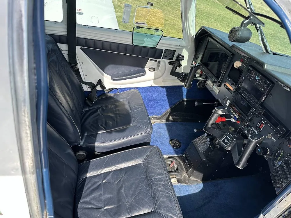 The aircraft's interior features dark blue leather seats and blue carpet, with the instrument panel visible in the foreground.