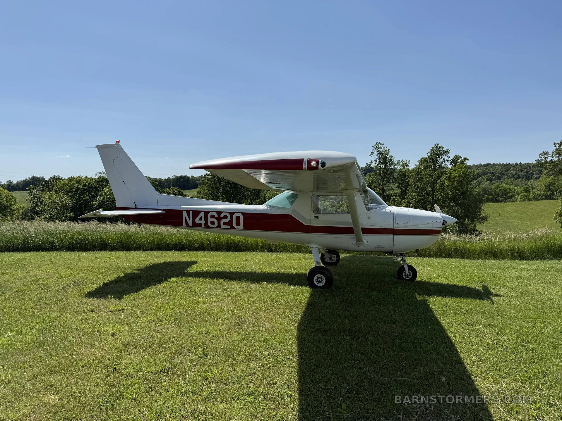 A white and red Cessna 150 is parked on a grassy field under a clear blue sky.
