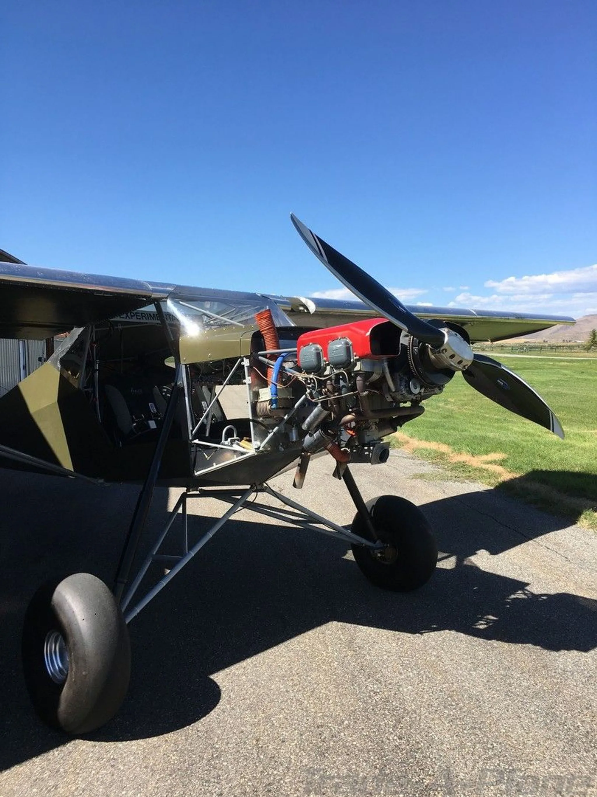 Front quarter view of the green experimental aircraft with its engine exposed, parked on an airfield.