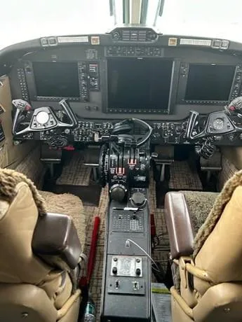 The cockpit of a private aircraft shows a modern instrument panel with multiple display screens and control yokes.