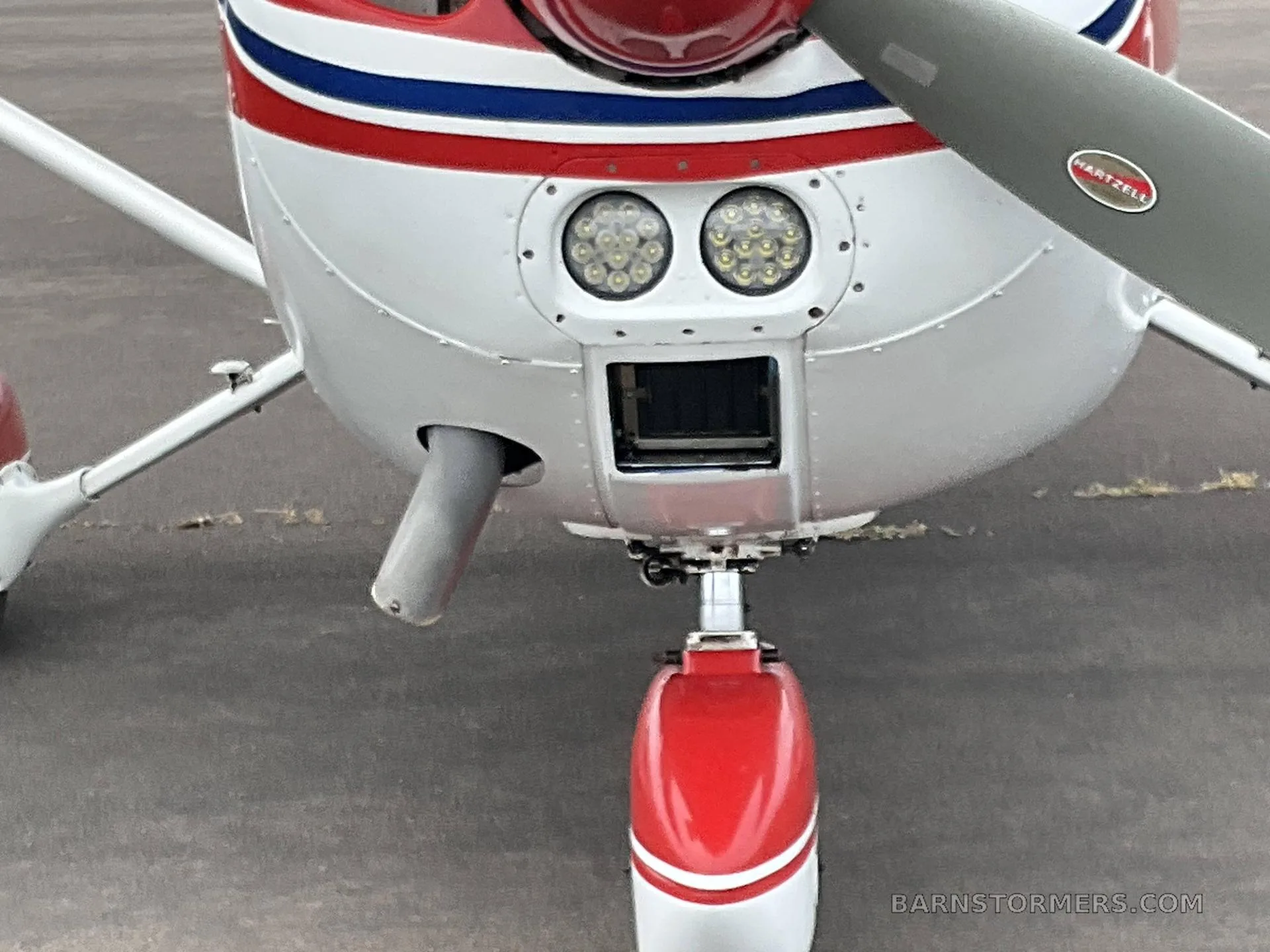 A close-up of the nose of a white and red Cessna 172 showing the propeller, landing lights, and nose gear.