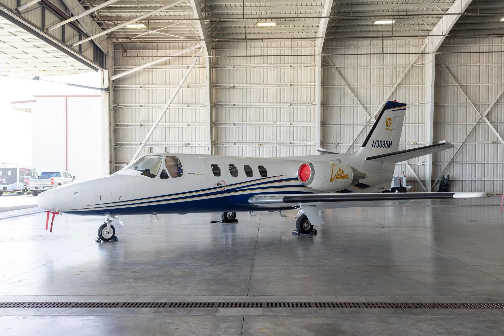 A white and blue Cessna Citation jet, registration N3095M, is parked inside a hangar.