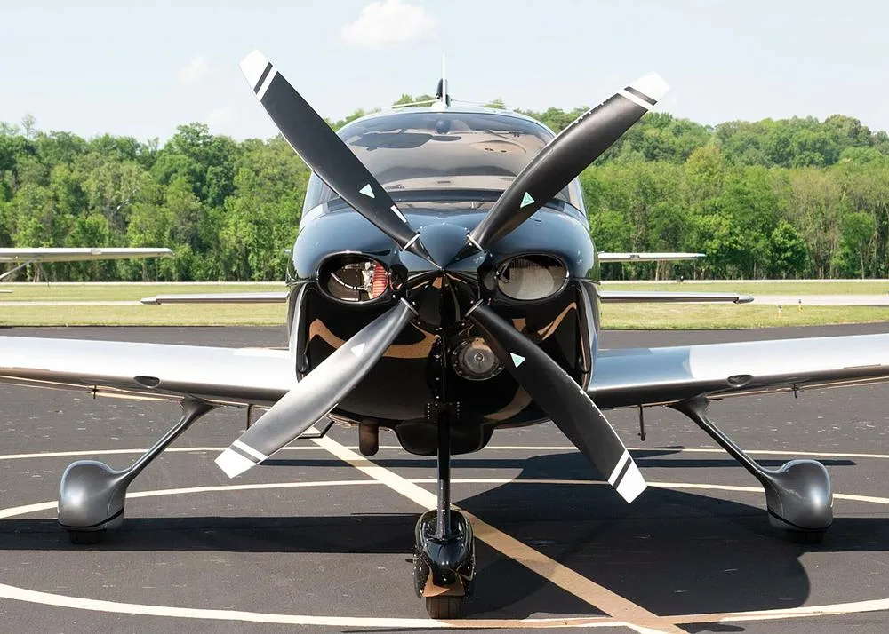 A close-up front view of the black and silver Cirrus SR22 aircraft N816RJ, highlighting its propeller and landing gear on an airfield.