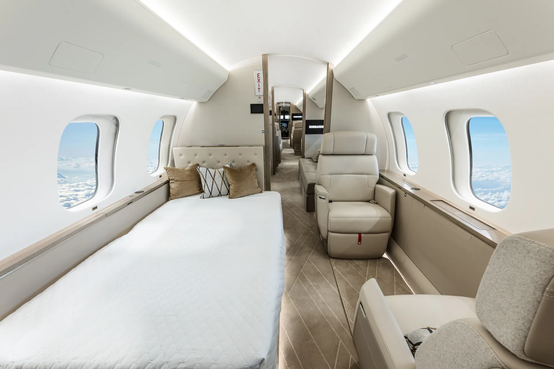 A private jet cabin configured with a bed on the left and a single cream leather seat on the right, with a Bombardier screen visible.