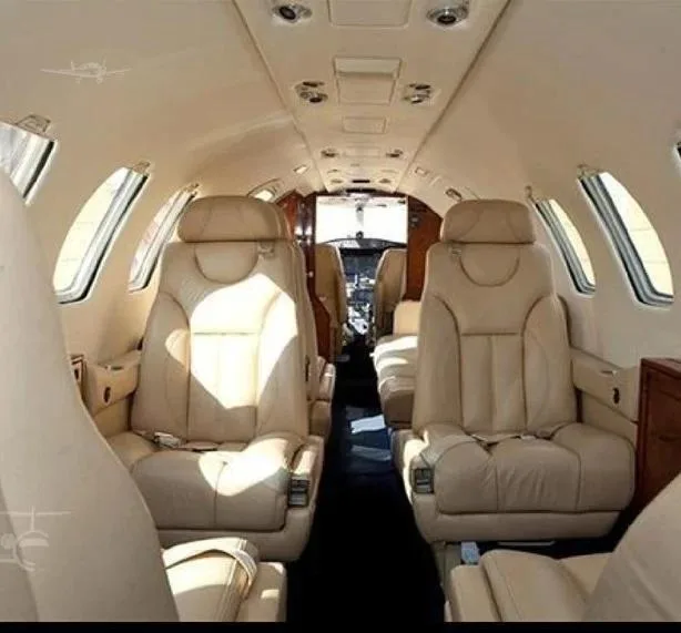 The aircraft's interior cabin features beige leather seats and a central aisle looking towards the cockpit.