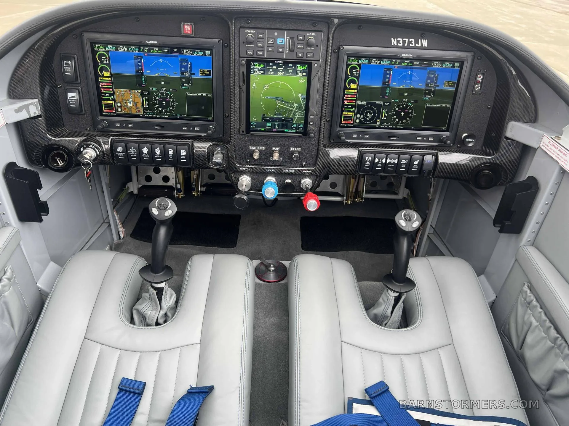 The cockpit of a light aircraft, featuring three large Garmin G3X Touch displays, dual stick controls, and grey leather seats.
