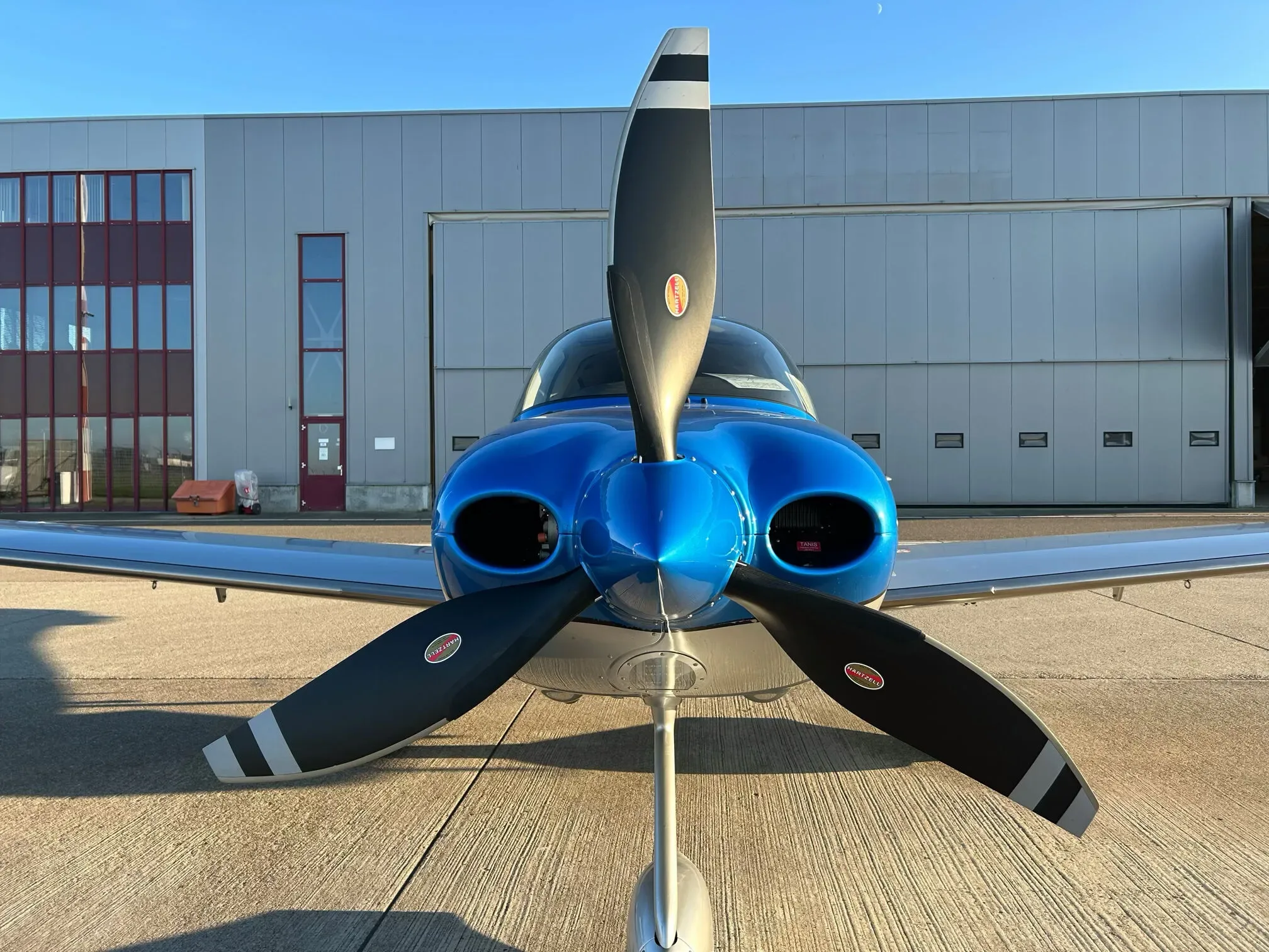 A head-on view of a blue and silver Cirrus SR22 aircraft showing its propeller and engine air intakes.