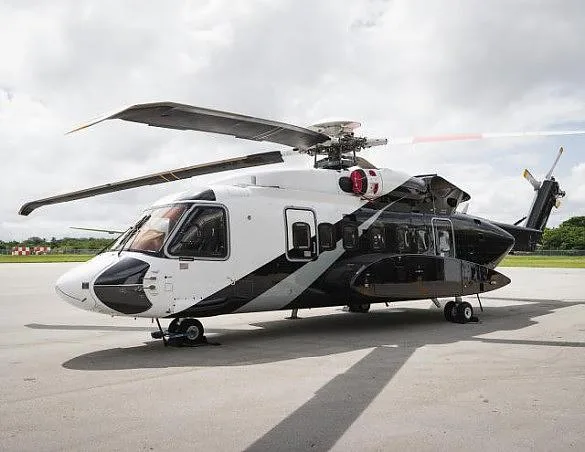 A white and black helicopter with its main rotor blades extended, parked on an asphalt surface under a cloudy sky.