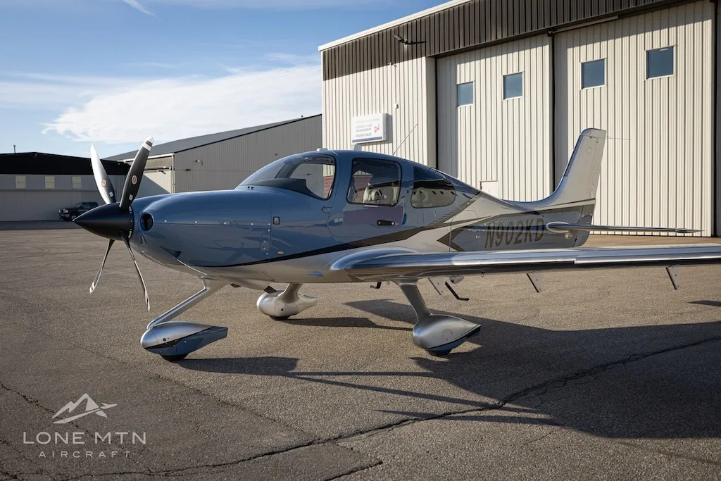 A front-side view of the Cirrus SR22T aircraft, N902KD, in blue and silver, parked on an airfield.