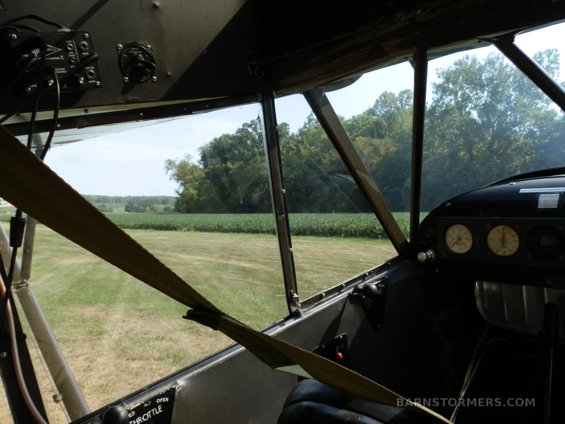 View from inside a small aircraft cockpit, showing the instrument panel, controls, and a field outside the windshield.