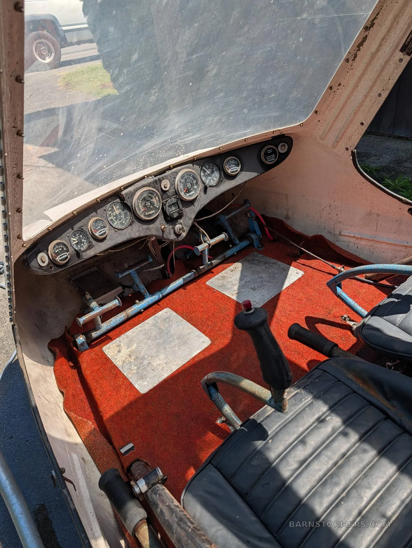 The cockpit of an experimental helicopter with an orange carpeted floor, a black instrument panel, and a control stick.