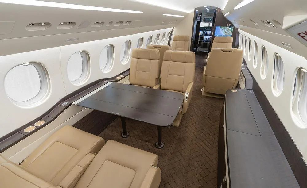 A wide view of the business jet's interior cabin with tan leather seats, a dark table, and a glimpse of the cockpit.