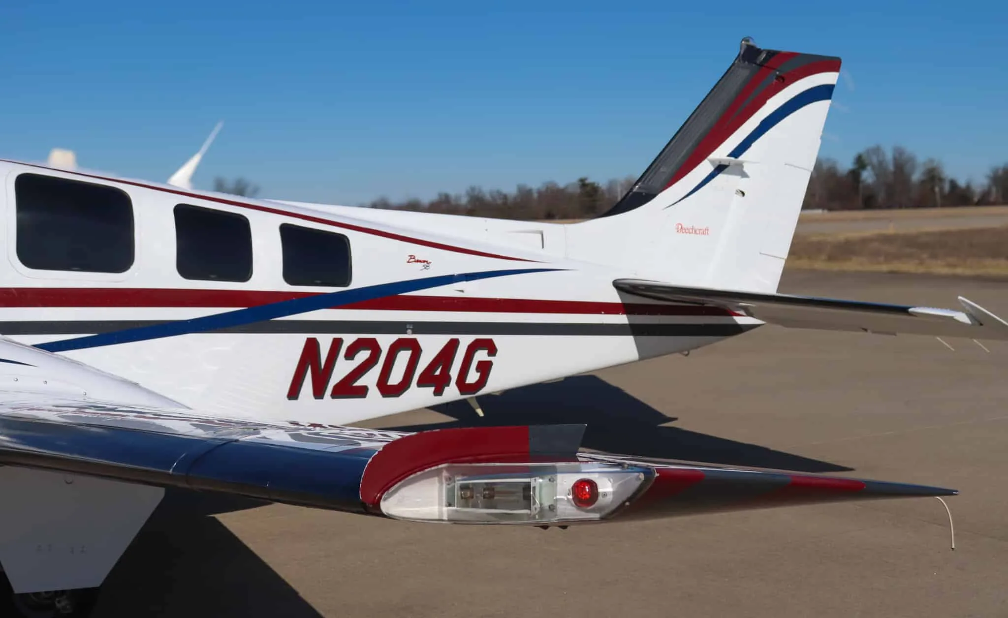 Close-up of the tail and right wing of a white Beechcraft Baron N204G, showing the red, blue, and gray stripes and navigation light.