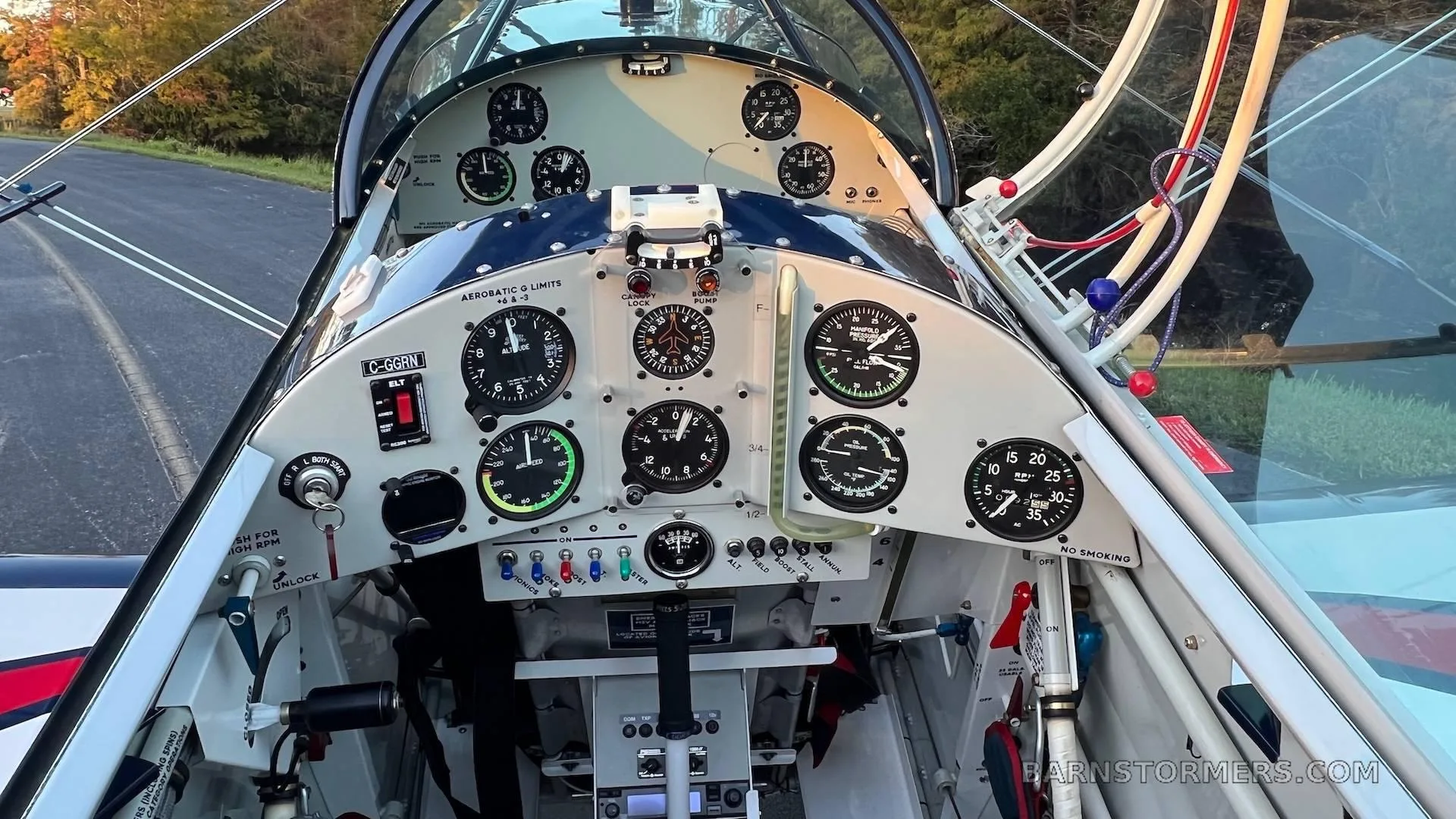 The cockpit of a biplane shows a white instrument panel with various gauges and controls.