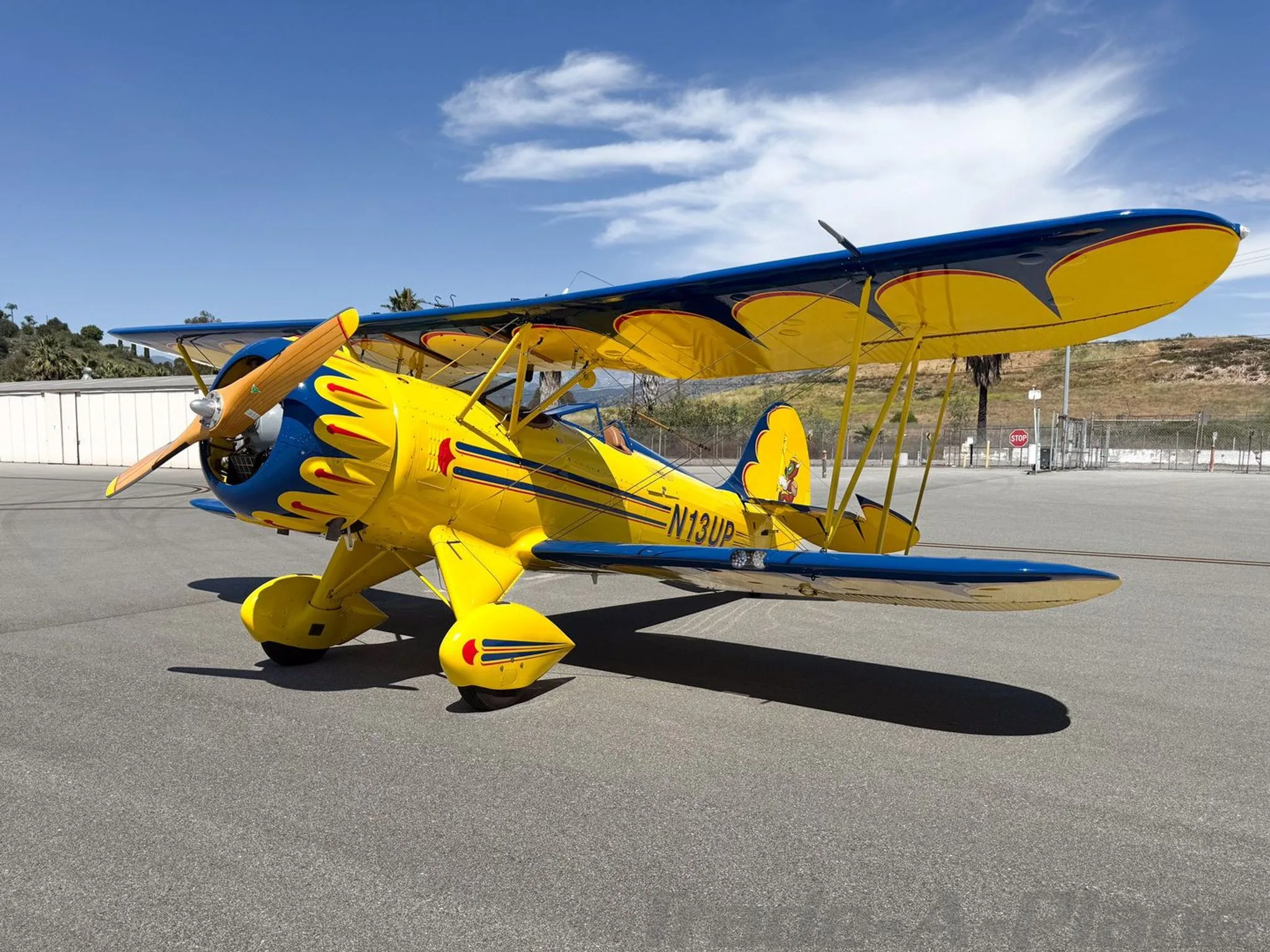 A yellow and blue biplane with red flame accents and registration N13UP parked on an airfield.