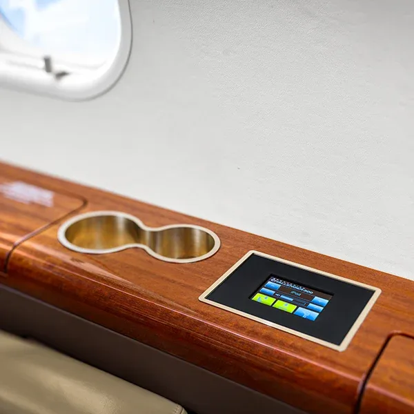A close-up of a polished wooden side panel in an aircraft cabin, showing a control screen and cup holders.