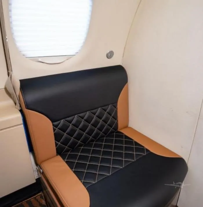 A close-up of a single tan and black quilted leather seat in the cabin of an Embraer Phenom 100.