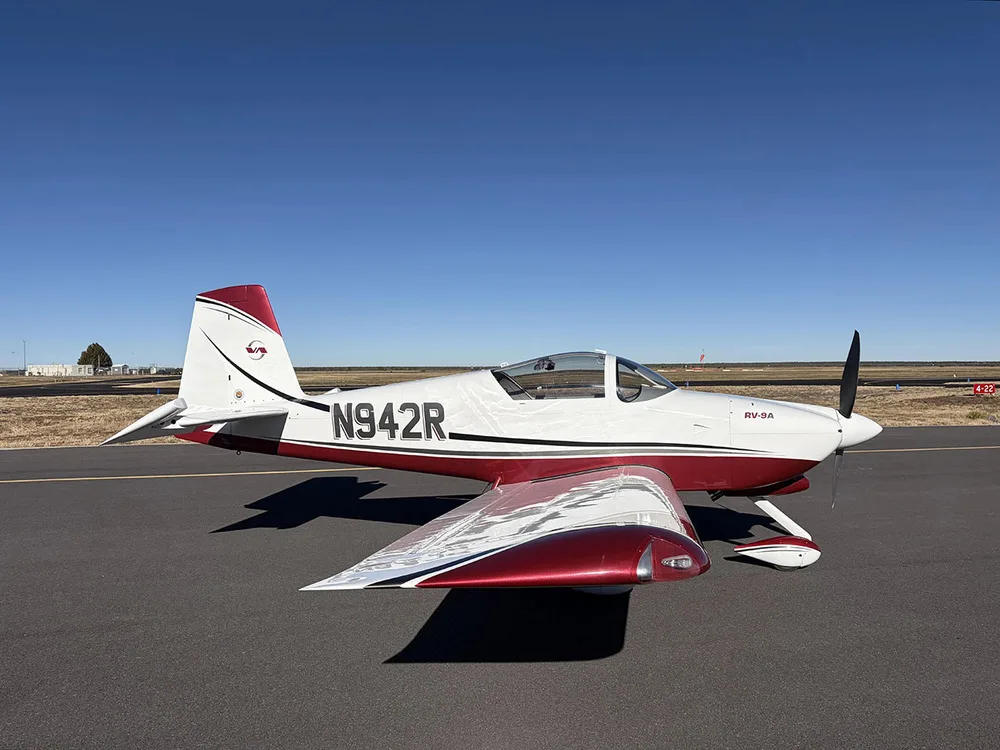 A three-quarter side view of the white and red Van's RV-9A aircraft N942R parked on an airfield.