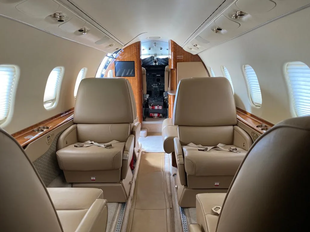 The luxurious interior cabin of a private jet, featuring beige leather seats and polished wood accents.