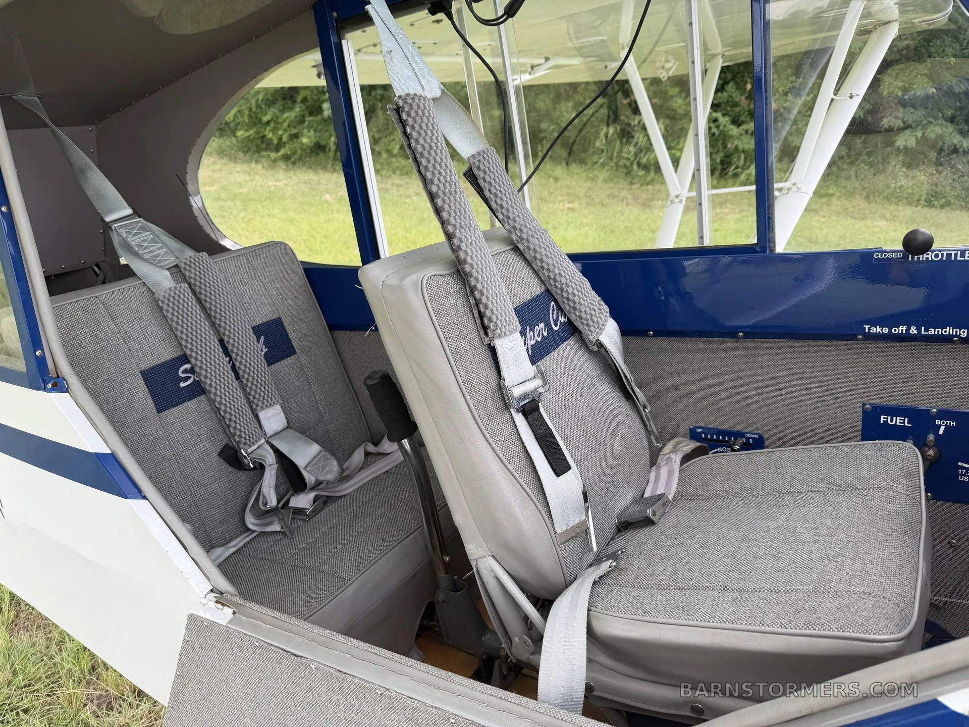 The gray fabric interior of a small aircraft cabin with two seats and seatbelts.