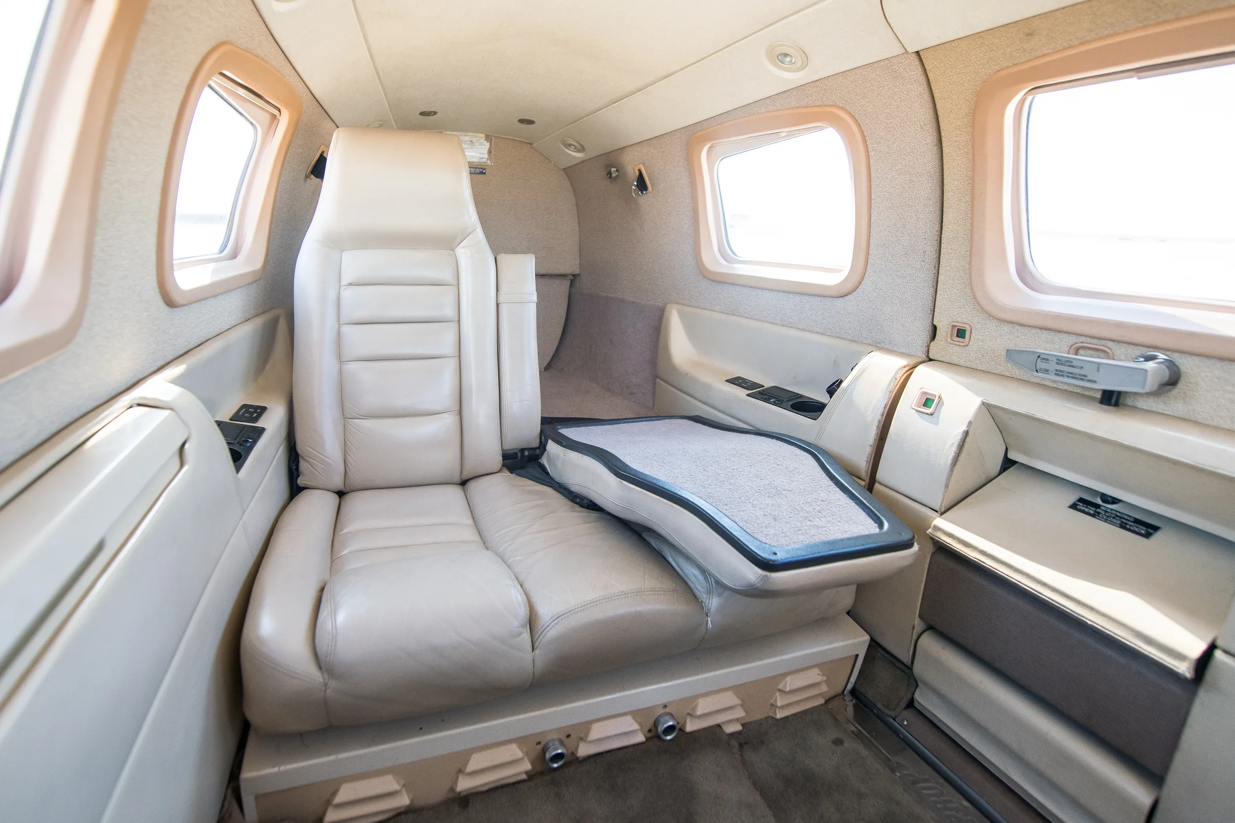 The beige leather interior of the N529WM aircraft cabin, showing a single seat with a fold-out table and windows.
