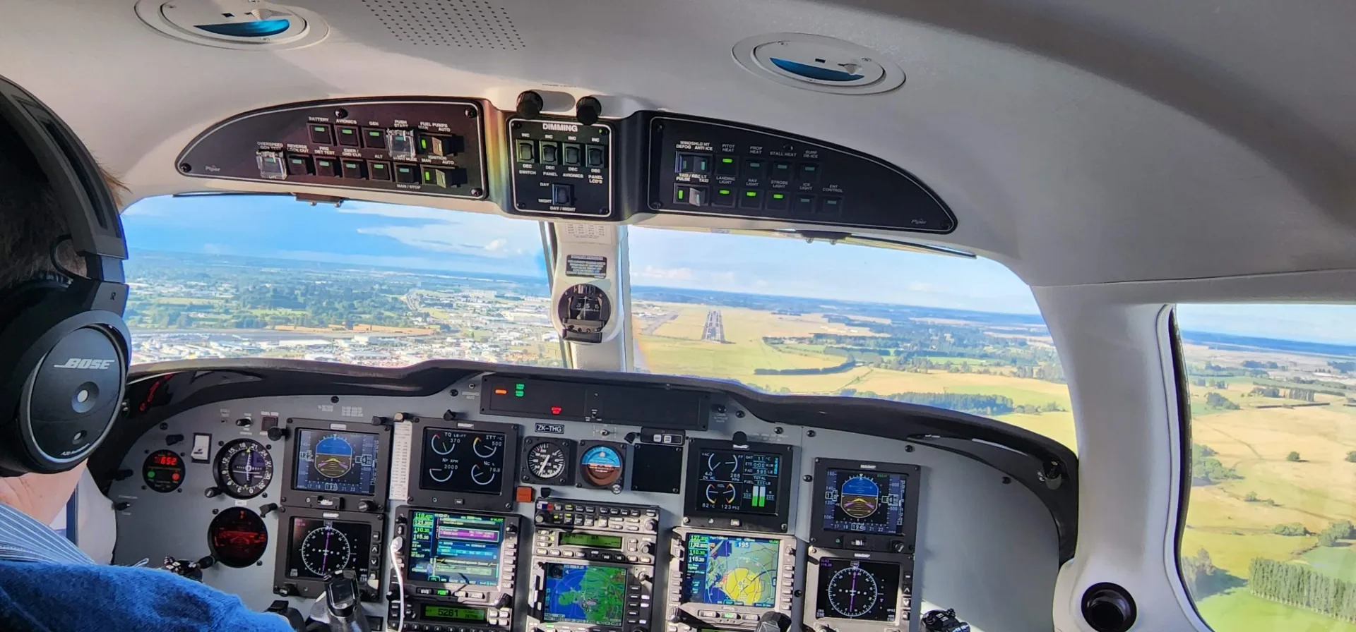 View from the cockpit of an aircraft, showing the instrument panel with multiple screens and a runway in the distance.