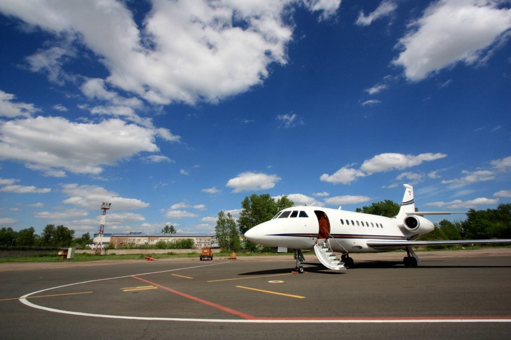 A silver Embraer Phenom 300 in flight against a blue sky.