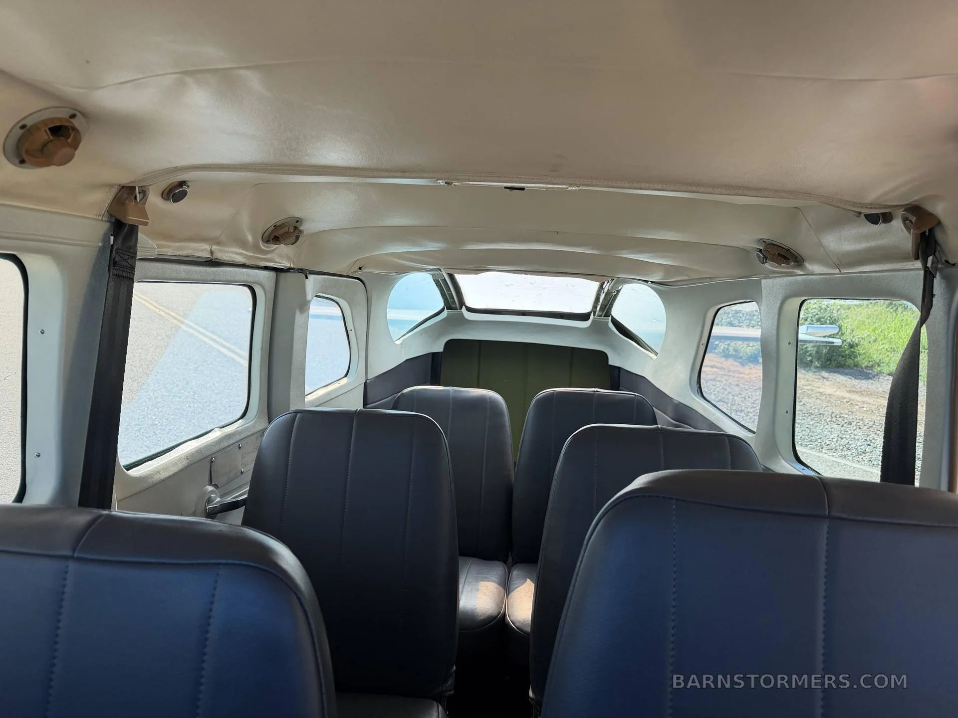 The aircraft cabin interior viewed from the rear, showing rows of dark seats and windows.