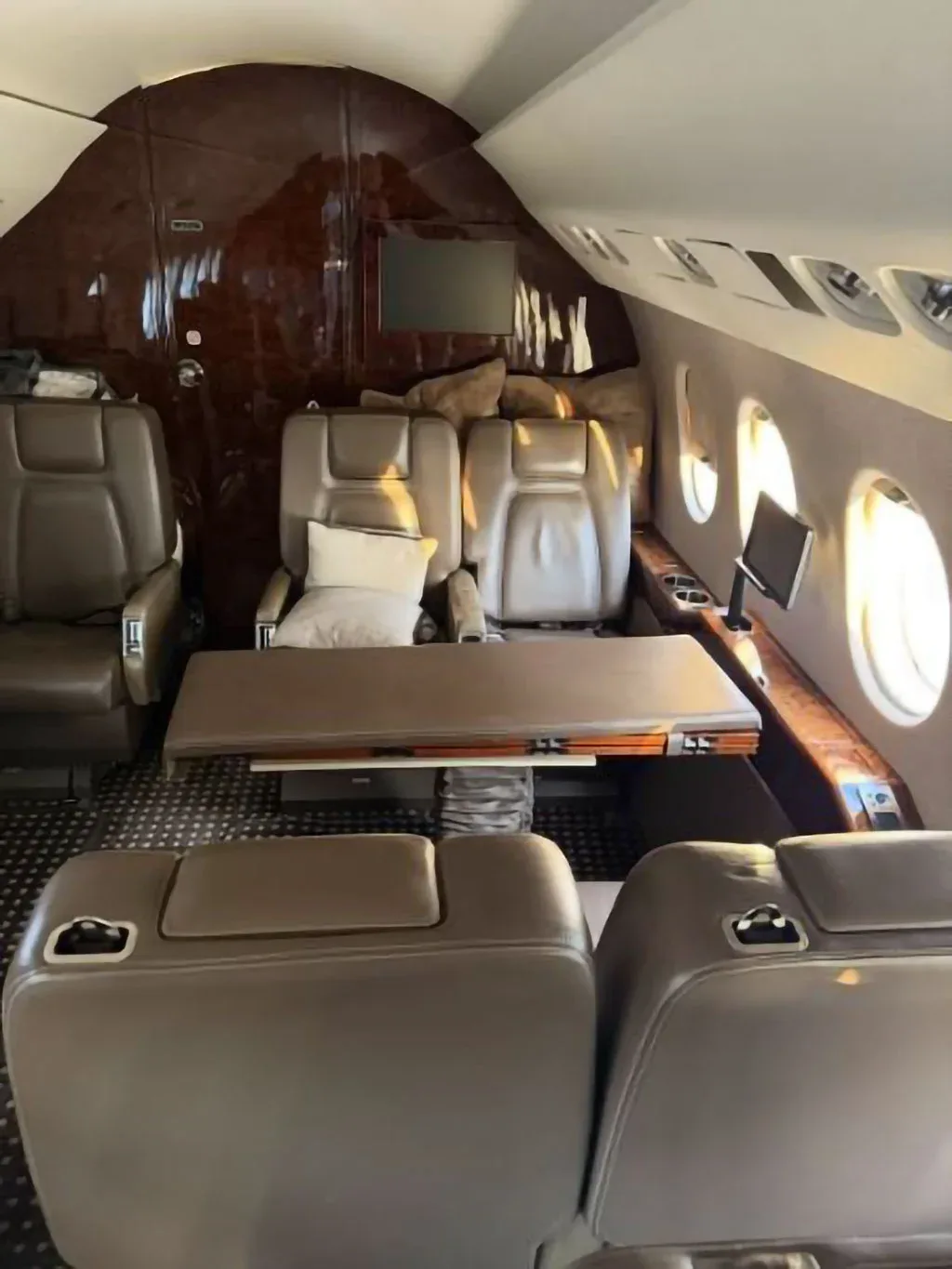 A spacious aircraft cabin interior featuring brown leather seating, a large table, and wood paneling.