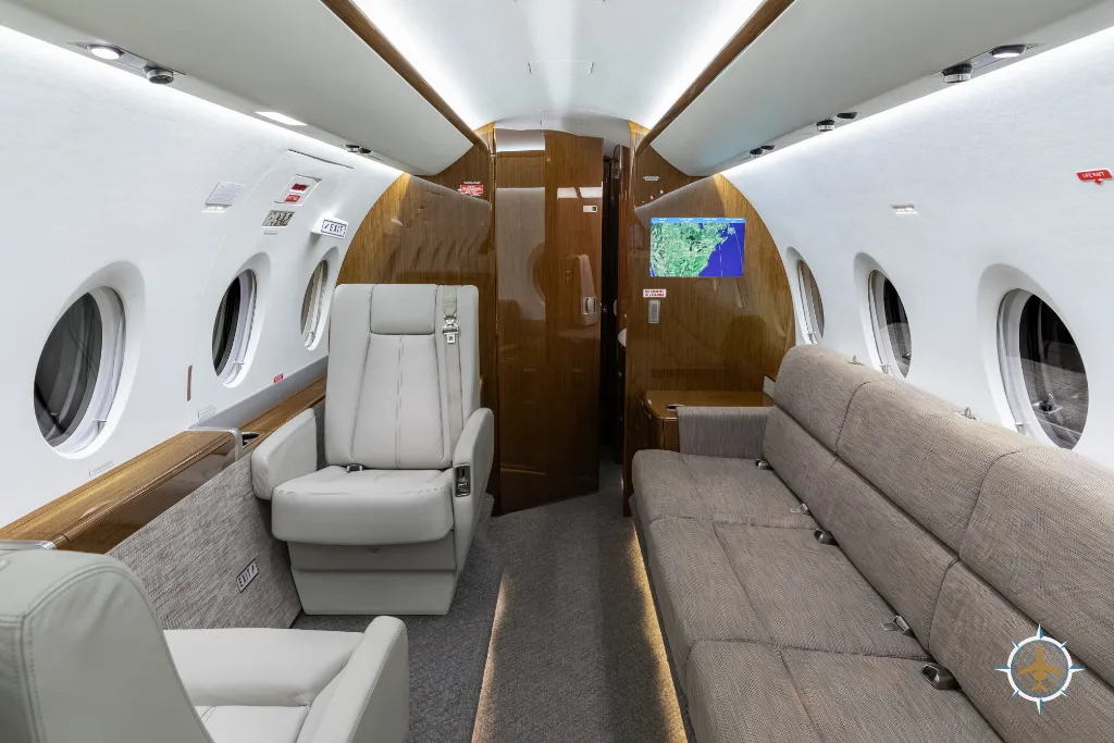The business jet cabin interior, looking towards the rear, with a single light grey seat and a long beige sofa.