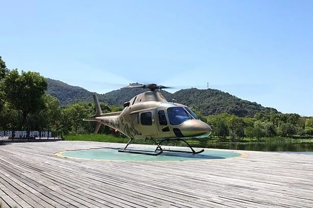A tan and camouflage-painted helicopter with skids sits on a vast concrete pad under a clear blue sky.