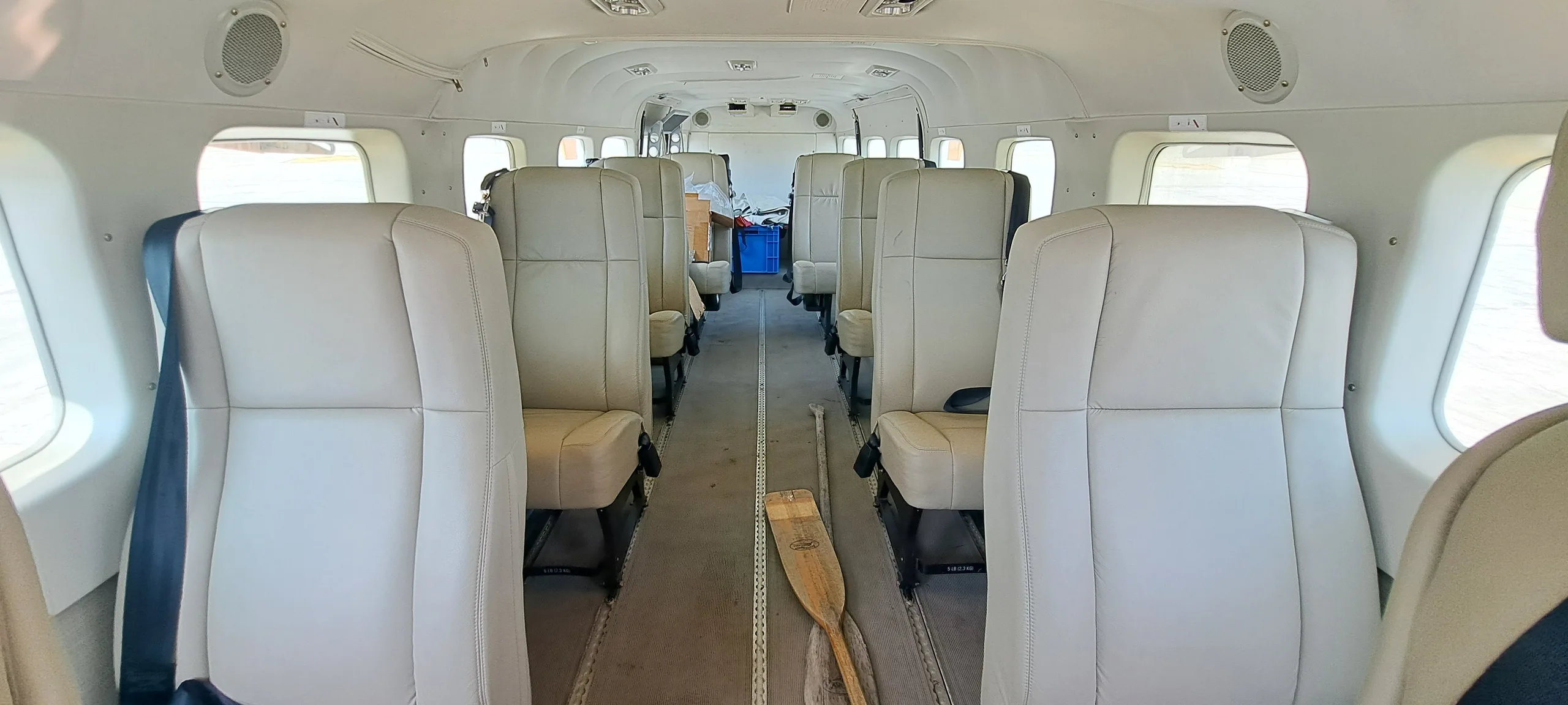 The interior cabin of an aircraft features rows of light-colored passenger seats and an oar on the floor.