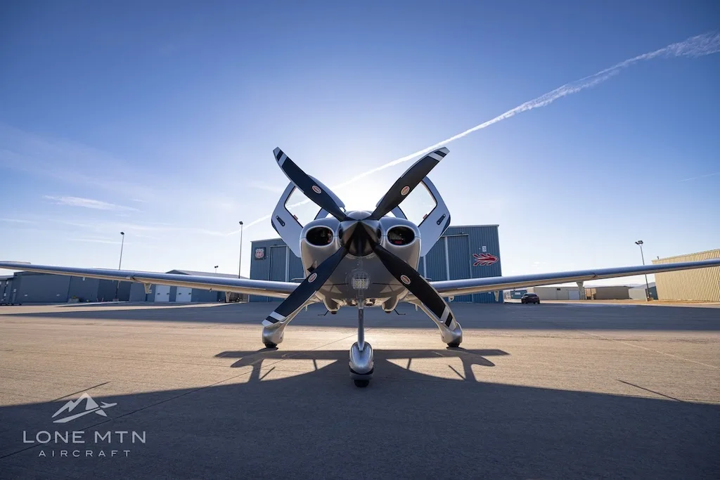 A head-on view of the silver Cirrus SR22T aircraft N221FS with its doors open, parked on an airfield.