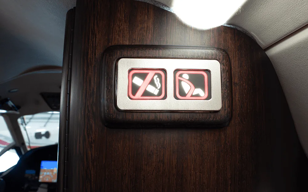 A close-up of illuminated "no smoking" and "fasten seatbelt" signs on a dark wood panel inside an aircraft.
