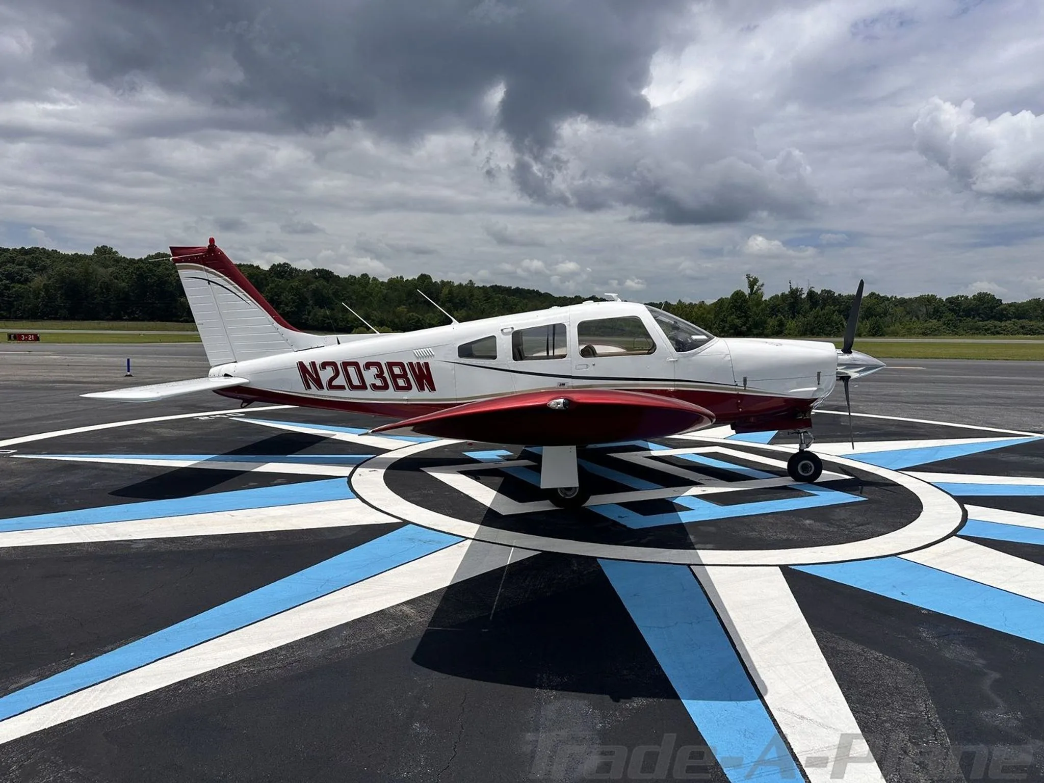 A white and red single-engine propeller aircraft, N203BW, parked on a tarmac with a compass rose marking.