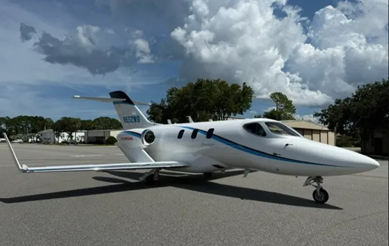 A white HondaJet HA-420 with blue accent stripes, registration N552WS, parked on an airfield under a partly cloudy sky.