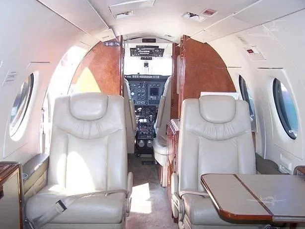 The aircraft's cabin interior features light-colored leather seats and wood paneling, looking towards the cockpit.