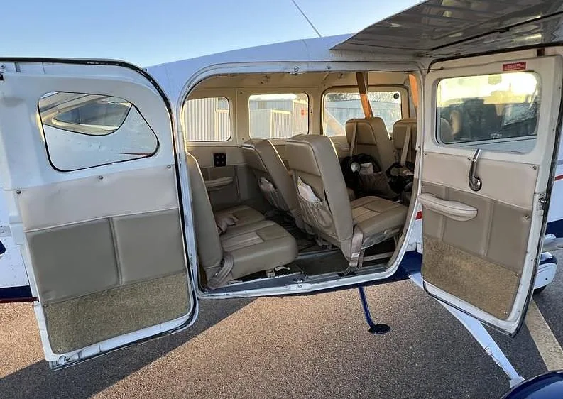The interior cabin of the Cessna 182 showing multiple rows of beige seats and open doors.