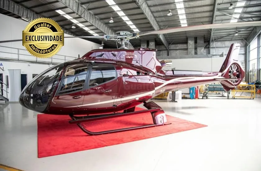 A burgundy helicopter with white stripes on a red carpet inside a hangar.
