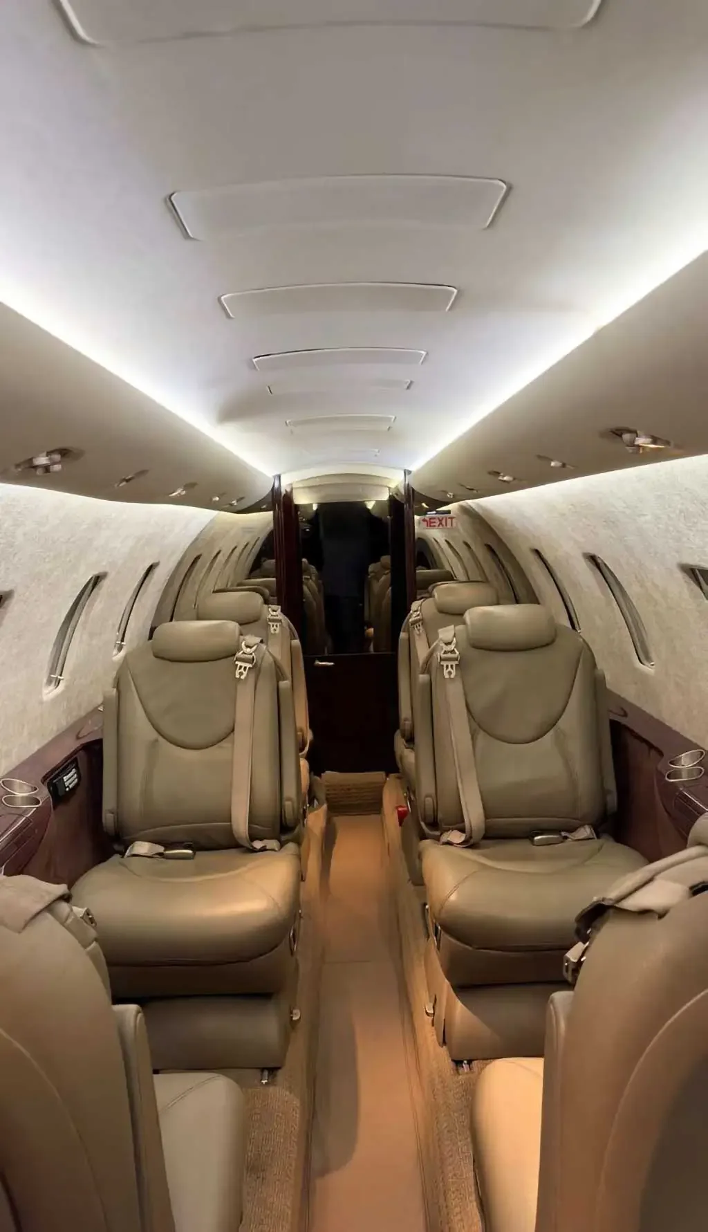 A slightly wider view of the aircraft cabin interior with beige leather seats and folded wooden tables, facing the rear of the cabin.