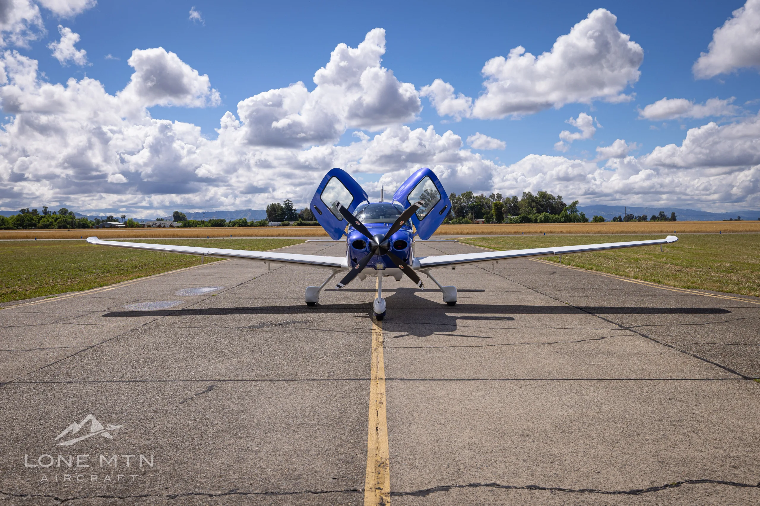 A blue and white Cirrus SR22 aircraft with its doors open, viewed from the front on an airfield.