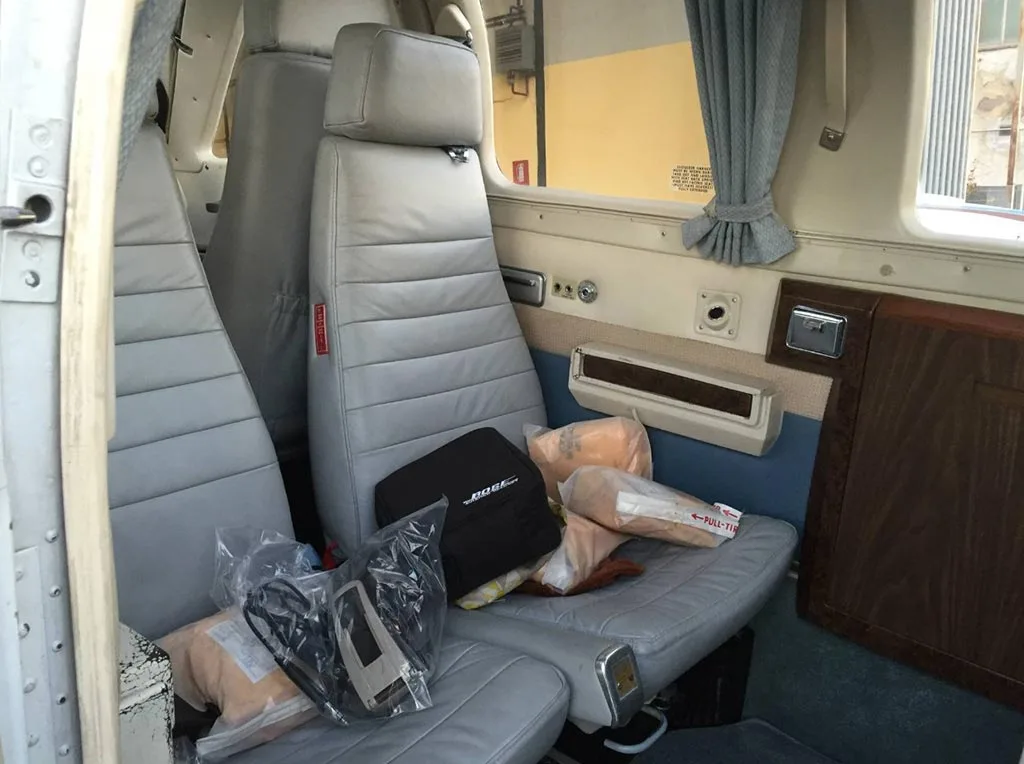 Interior view of an aircraft cabin with light gray leather seats and various items on the seats.