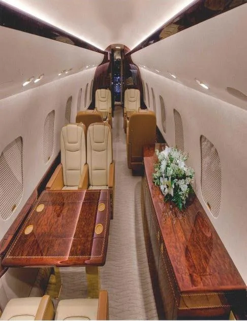 A long view of a private jet's luxurious cabin with a dining table, comfortable seating, and a side console with flowers.