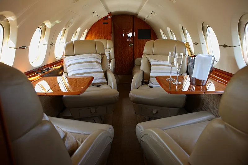 A luxurious aircraft interior with tan leather seats, wooden accents, and champagne flutes on a table.